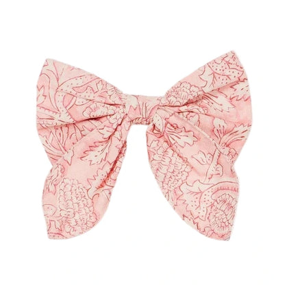 The Louise Misha Gilla Hair Clip is a pink fabric bow with a floral pattern, two wide loops, and angled tails—perfect as a charming floral accessory.