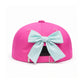 The Dolphin Daydream Bow Hat by Bits & Bows is a bright pink kids’ baseball cap, featuring a blue and white seersucker bow attached at the back, displayed on a white background.