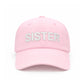 A light pink Sister Bow Hat by Bits & Bows, featuring “SISTER” embroidered in large white letters on the front and an adjustable tuckstrap for a comfortable fit—perfect for celebrating sisterhood in style.