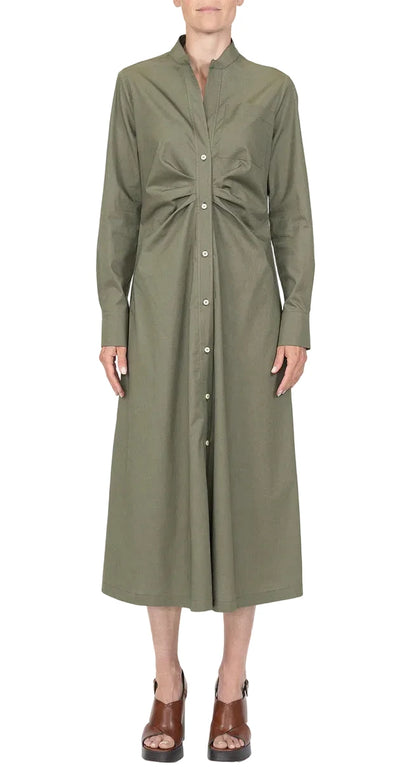 A person wearing the Genny Dress by Callas Milano, a long sleeve button front dress in olive green Italian shirting twill with a gathered waist, paired with brown open-toe sandals.