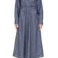 A woman wears the Genny Dress by Callas Milano—a blue chambray, long-sleeve, button-front piece with a fitted waist and classic fit-and-flare silhouette—styled with brown open-toe platform sandals.