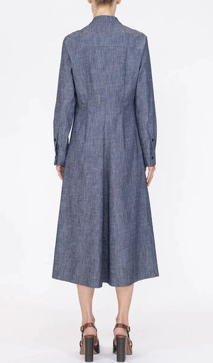 A person is shown from the back against a plain white background wearing the Callas Milano Genny Dress, a blue chambray long sleeve button-front style, paired with brown heeled sandals.