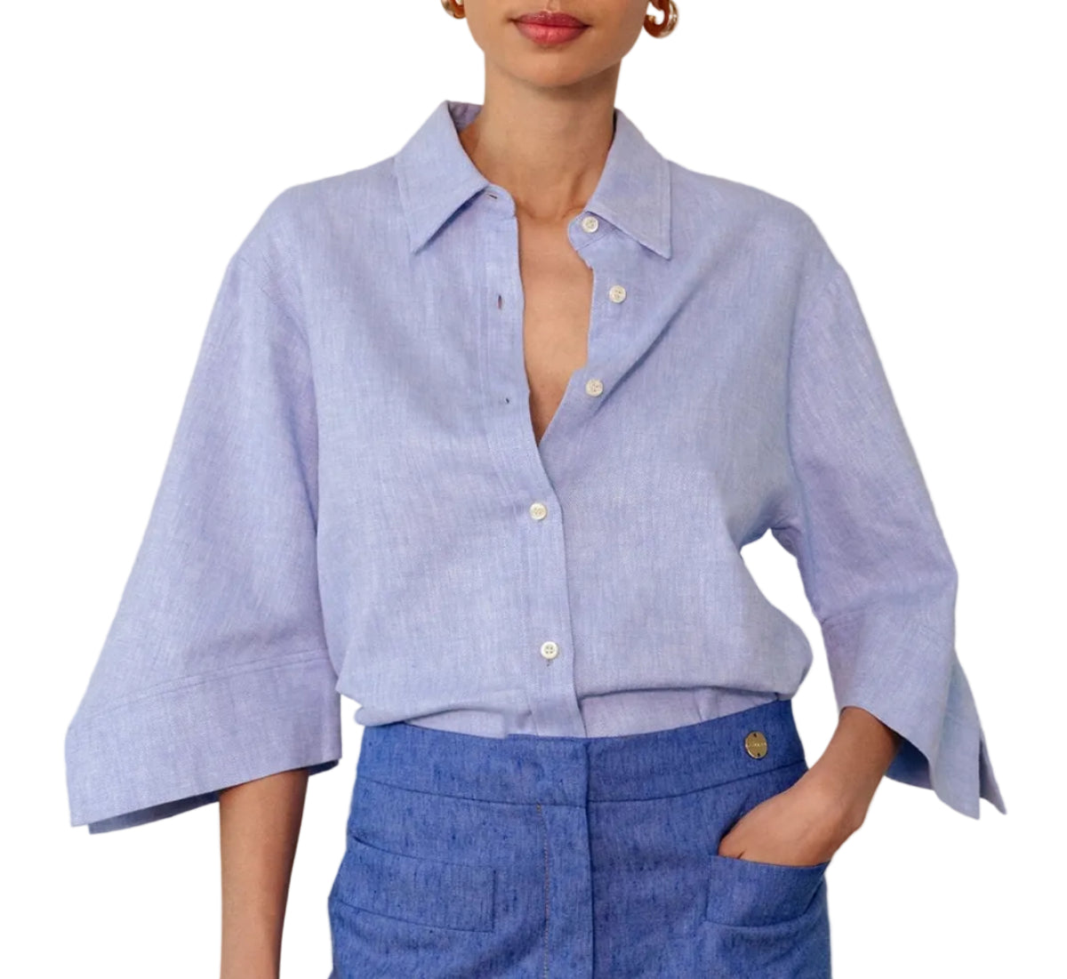 A woman wears the Georgie Top by Callas Milano, a classic light blue Italian twill shirt with a point collar and wide sleeves, tucked into high-waisted textured blue pants.
