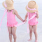 Two young children in matching Youth Harbor Hats by Bits & Bows hold hands in shallow beach water, enjoying both style and sun protection.