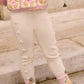 A child wearing Louise Misha Baby Girls' and Girls' Molda Leggings with an elasticized waist stands on stone steps, paired with pink and green socks, brown sandals, and a pink crochet sweater.
