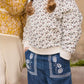 A child in a white floral sweatshirt and Louise Misha Girls' Flofi Pants with an elastic waist stands next to another child wearing a yellow patterned jacket.