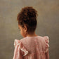 A young child with curly hair, wearing the Louise Misha Girls' Saralou Dress in pink cotton gauze with ruffled sleeves, stands facing away from the camera against a neutral background.