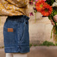 A child stands next to a person holding a bouquet of colorful flowers, wearing a patterned yellow top, white tights, and Louise Misha Girls' Virgina Shorts with a wide fit and elasticized waist.