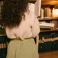 A child with curly hair, wearing a cream sweater and the Louise Misha Girls' Cephee Skirt—a green corduroy skirt with an elasticized waistband—stands in front of bookshelves reading an open book.
