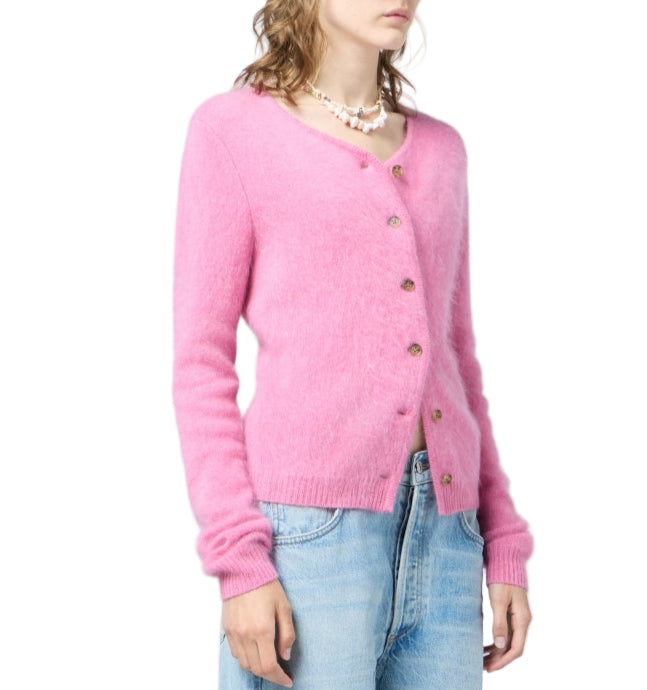 A person wears the Grizzly Cashmere Cardigan by Guest in Residence in fuzzy pink, paired with light blue jeans and layered necklaces, set against a white background.