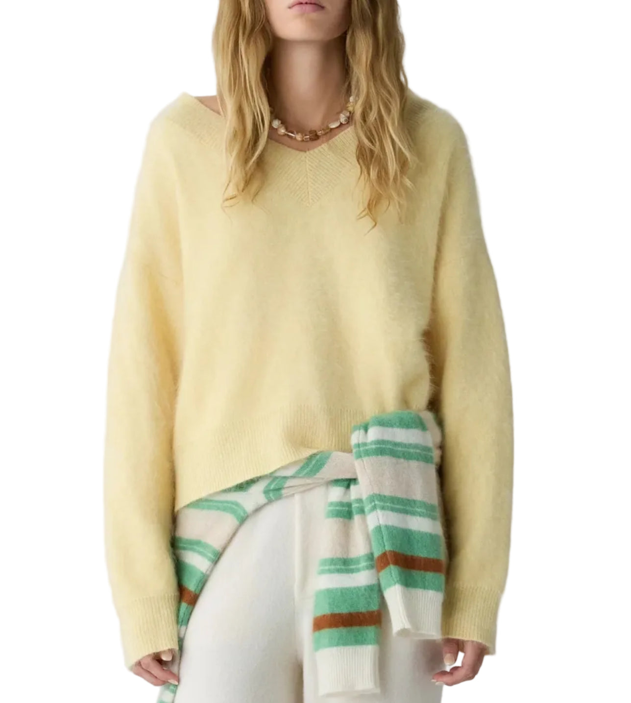 A woman wearing the Grizzly Double V Sweater by Guest in Residence in yellow, styled loosely with white pants and a striped sweater tied around her waist.