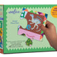 A hand holds a dinosaur puzzle piece in front of a green Eeboo Dinosaur Alphabet 20 Piece Puzzle box, which features colorful artwork and shows the puzzle’s size for children learning.