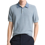 A person wears the Vince Geo Jacquard Shortsleeve Polo in light blue with dark trousers, standing against a plain white background.