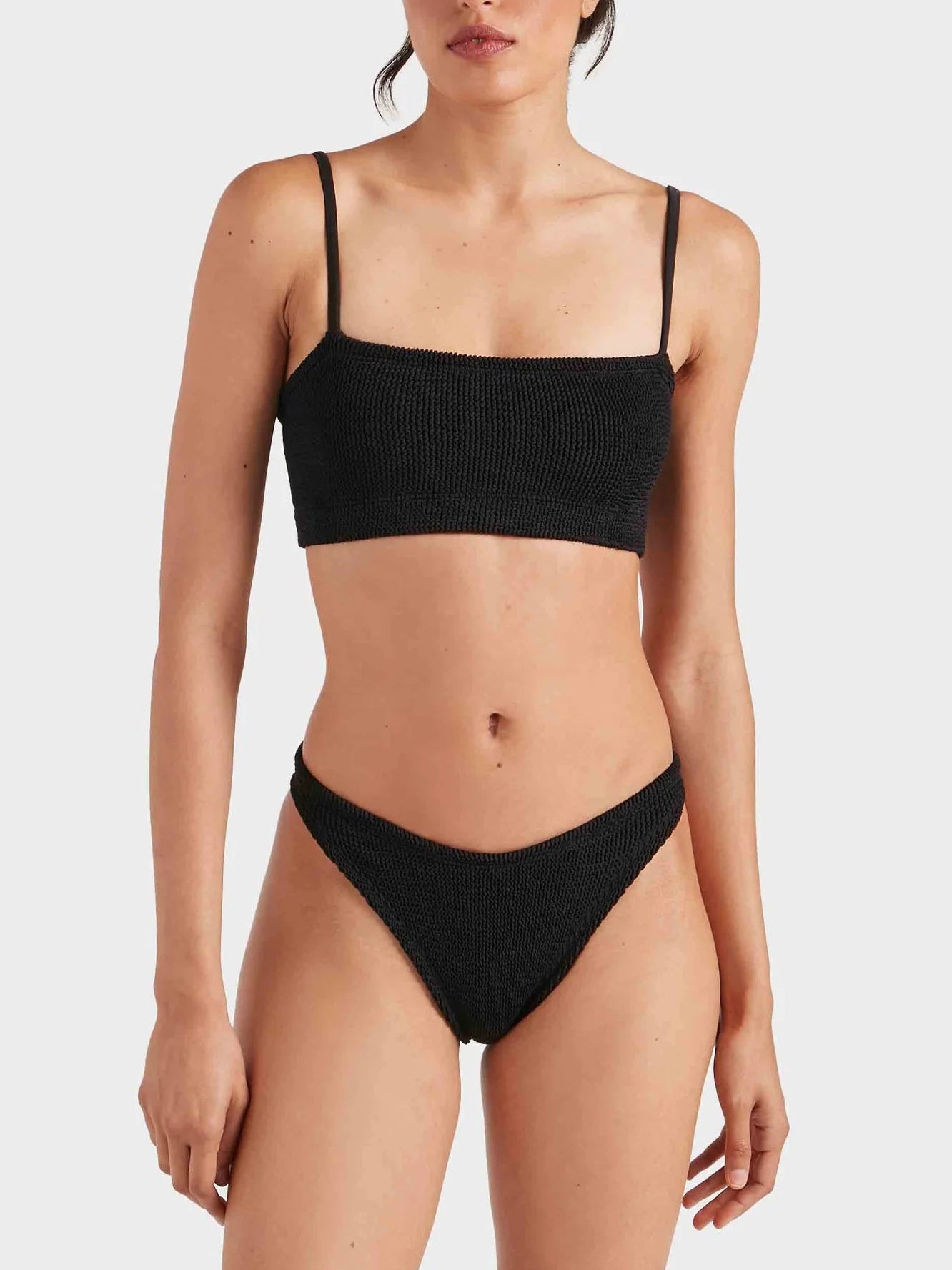 A woman wears the Hunza G Gigi Bikini in black crinkle fabric, featuring a straight neckline top and high-cut bottoms, against a plain light background.