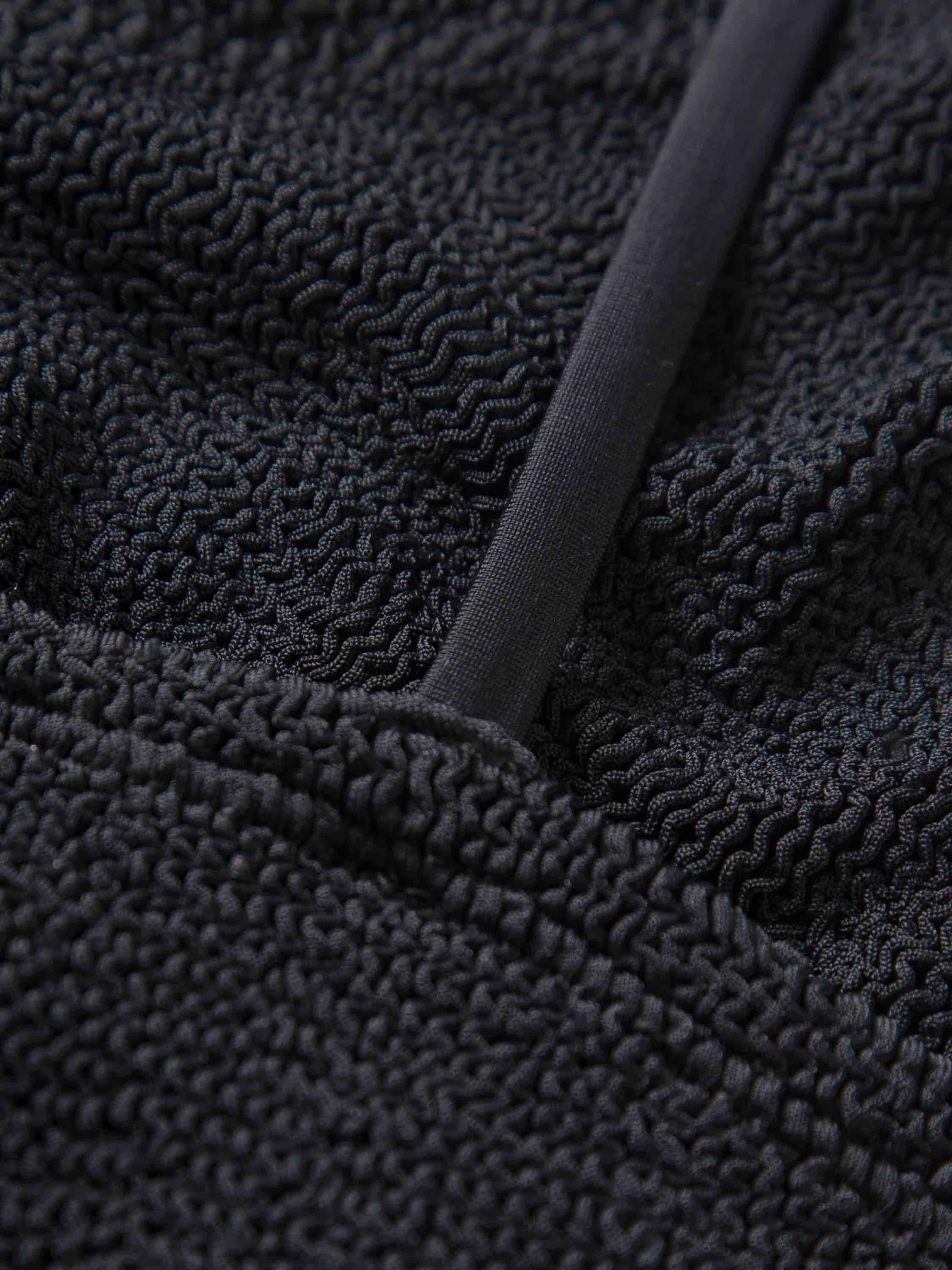 Close-up of the Gigi Bikini by Hunza G: black crinkle fabric with a raised, wavy pattern and a smooth, diagonal strap—ideal for a stylish one-size swimsuit look.