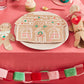 A festive holiday feast comes to life with the Meri Meri Gingerbread House Plates, complemented by delightful gingerbread man decorations, a cupcake, and a red-green paper chain gracefully placed on a pink tablecloth. Ideal for your Christmas party celebration!