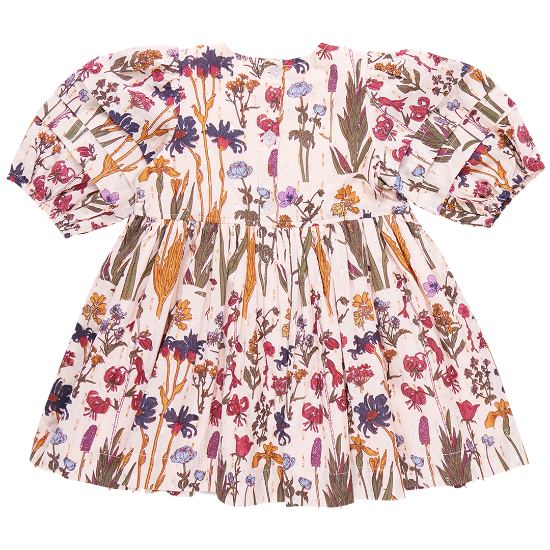 The Pink Chicken Girls' Brooke Dress is a short-sleeved dress adorned with a floral pattern showcasing various flowers in shades of pink, purple, and yellow on a white background. It features gathered puff sleeves and a glitter button back closure that adds an extra touch of charm.