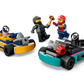 Two minifigures in racing outfits from the LEGO® Go-Karts & Race Drivers set by Legos - Toyhouse stand next to two colorful race cars, one vibrant yellow and the other a striking blue. One figure triumphantly raises the winner's trophy, celebrating an exciting victory in the thrilling world of LEGO racing.