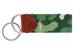 The Smathers & Branson Golfer's Camo Key Fob features an Italian leather tab with two metal rings. Its fabric strap is crafted with French cotton thread, showcasing a green camouflage pattern along with a small red and white flag design.