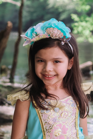 A little girl wearing a Great Pretenders Mermalicious Headband adorned with sequins and pearls.