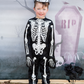 A child proudly stands in front of a Halloween-themed backdrop featuring an eerie tombstone design while wearing the Great Pretenders Glow in Dark Skeleton Set.