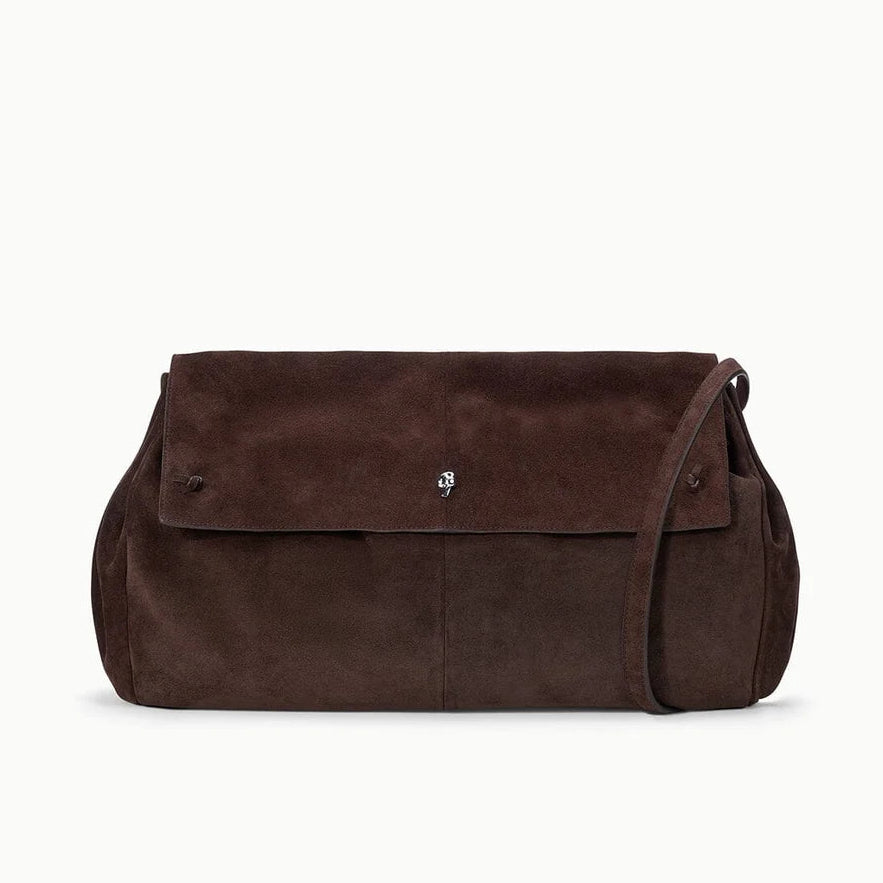 The Cy Oversized Bag by Staud is a brown suede shoulder bag featuring a flap closure, subtle logo detail on the front, and a long drop strap for versatile styling—displayed against a plain white background, this statement piece stands out.