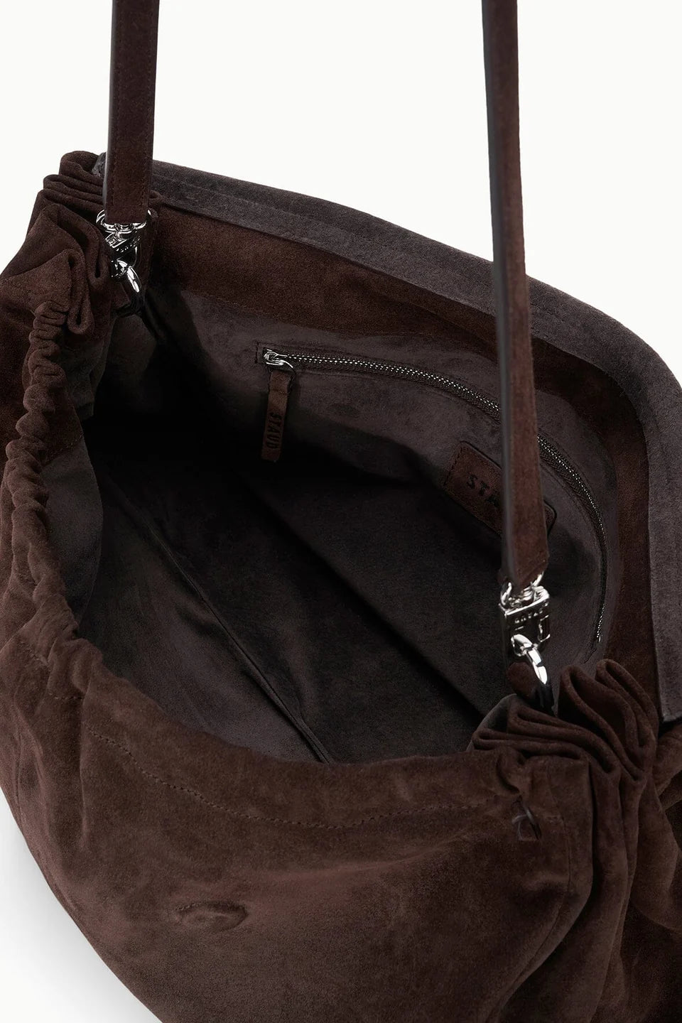 Close-up of the interior of the Staud Cy Oversized Bag in brown suede, featuring a zippered pocket, fabric lining, and two leather handles secured with metal hardware—a statement piece designed for both style and function.
