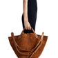 A person in a sleeveless black dress holds a Proenza Schouler Chelsea Large Soft Suede Tote, its rich brown suede enhanced by an adjustable shoulder strap.