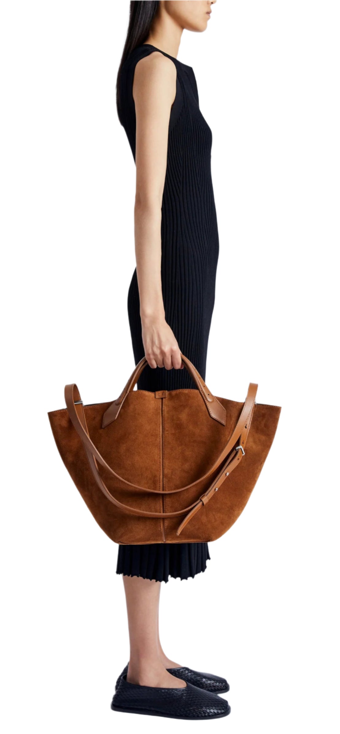 A person in a sleeveless black dress holds a Proenza Schouler Chelsea Large Soft Suede Tote, its rich brown suede enhanced by an adjustable shoulder strap.