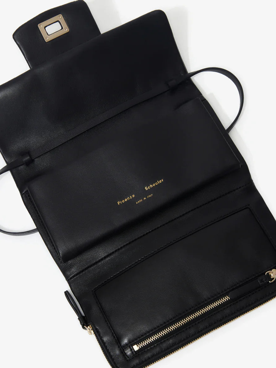 A Proenza Schouler Flip Shoulder Bag in black nappa leather features a PS1 closure and an open flap, revealing multiple compartments and a zipper pocket, with the brand name "Proenza Schouler" displayed in gold lettering.