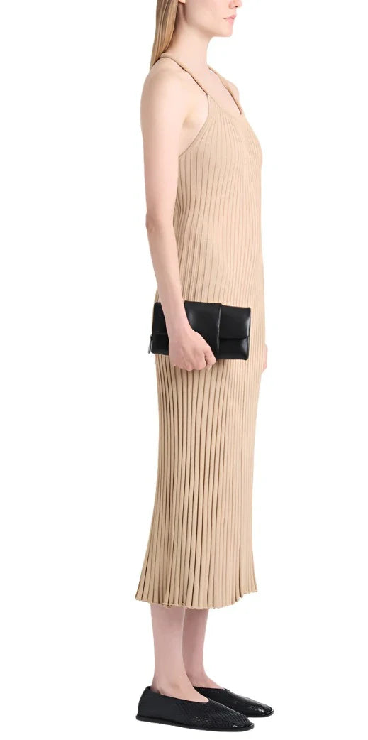 A woman is standing in a beige pleated dress, holding a Proenza Schouler Flip Shoulder Bag and wearing black flat shoes. She is facing sideways.