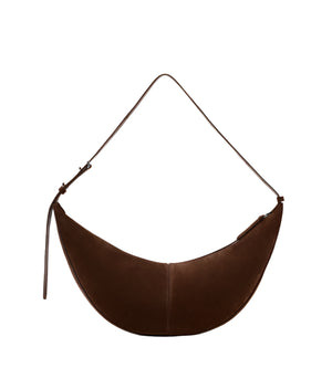 The Proenza Schouler Slide Suede Bag features a curved silhouette, adjustable strap, and brown suede design. Shown crescent-shaped against a plain white background.