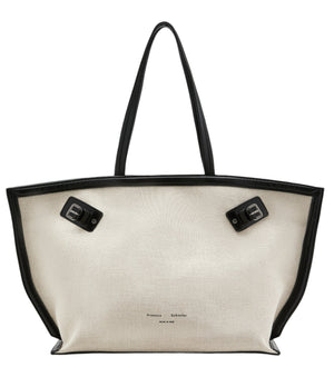 The Days Natural Linen Tote by Proenza Schouler is a spacious white linen carryall featuring black leather handles, trim, and base panel, accentuated with two sophisticated black buckles at the top.
