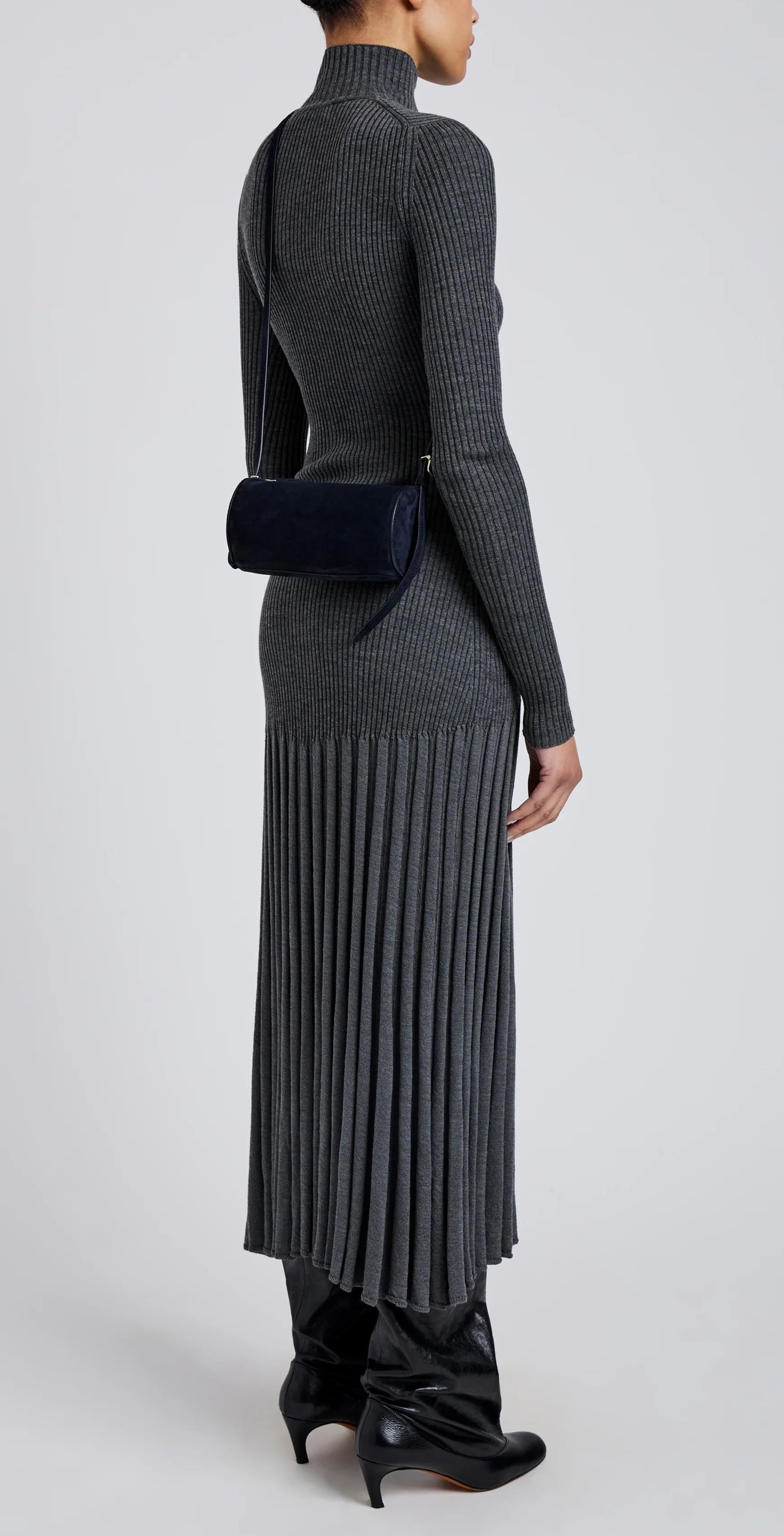 A person in a long, ribbed gray dress and black boots is shown from the back, carrying a Proenza Schouler Silo Crossbody Bag with an adjustable strap over their shoulder.