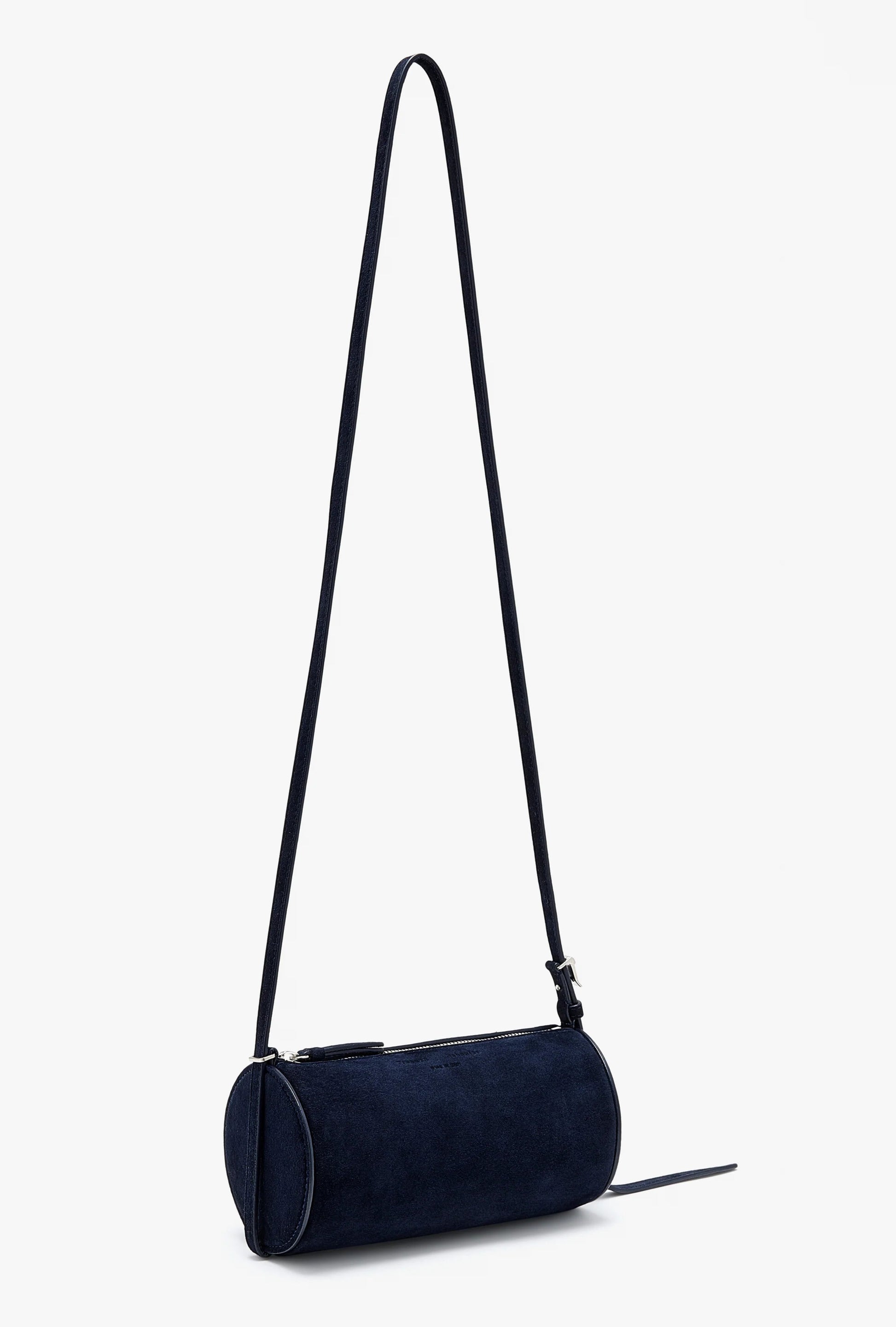 The Silo Crossbody Bag by Proenza Schouler, in dark blue suede with a long adjustable strap and zipper closure, is shown against a plain light background.