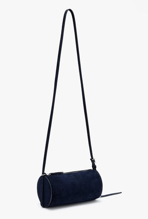 The Silo Crossbody Bag by Proenza Schouler, in dark blue suede with a long adjustable strap and zipper closure, is shown against a plain light background.
