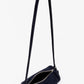 The Proenza Schouler Silo Crossbody Bag is a small black suede, cylindrical barrel bag with an adjustable strap and silver zipper, shown open against a plain white background.