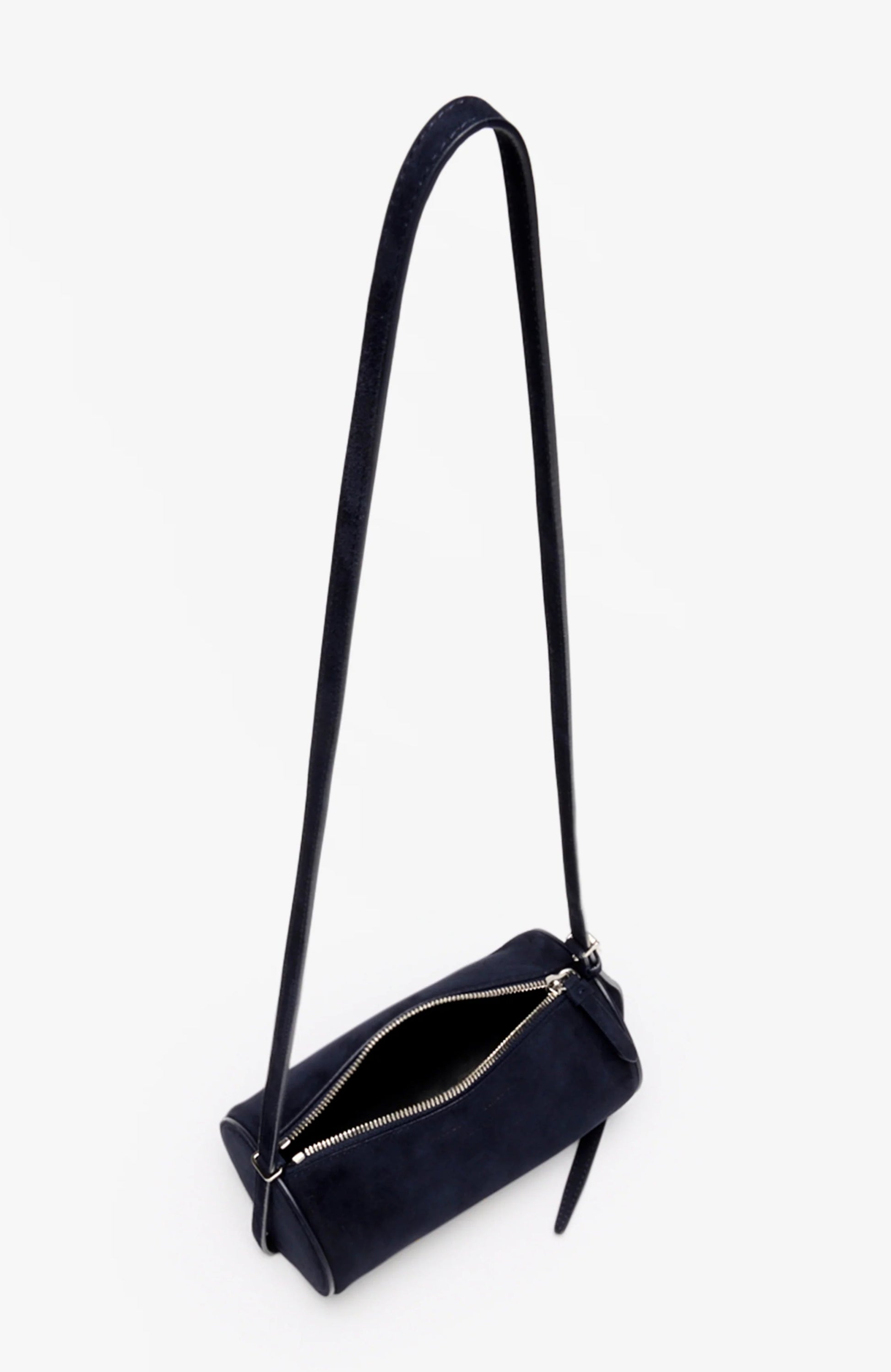 The Proenza Schouler Silo Crossbody Bag is a small black suede, cylindrical barrel bag with an adjustable strap and silver zipper, shown open against a plain white background.