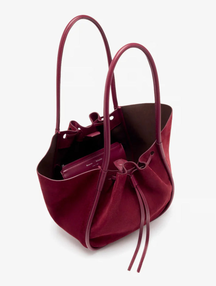 The Proenza Schouler Large Ruched Soft Suede Tote in burgundy features leather handles, a drawstring closure, matching wallet, and subtle gold-tone logo for an elegant finish.