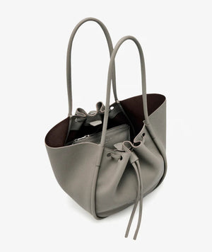 The Proenza Schouler Large Ruched Soft Pebbled Calf Tote in grey features double handles, a drawstring closure, and an inner leather zip pouch, displayed against a plain white background.