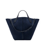 The Chelsea Large Soft Suede Tote by Proenza Schouler, shown in navy blue with two black leather handles and an adjustable shoulder strap, features an unstructured silhouette and is photographed on a white background.