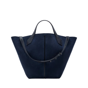 The Chelsea Large Soft Suede Tote by Proenza Schouler, shown in navy blue with two black leather handles and an adjustable shoulder strap, features an unstructured silhouette and is photographed on a white background.