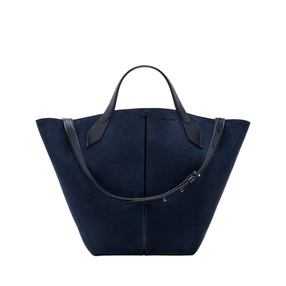 The Chelsea Large Soft Suede Tote by Proenza Schouler, shown in navy blue with two black leather handles and an adjustable shoulder strap, features an unstructured silhouette and is photographed on a white background.