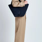 A person in a beige suit stands in profile with the Proenza Schouler Chelsea Large Soft Suede Tote over their shoulder against a plain light background.