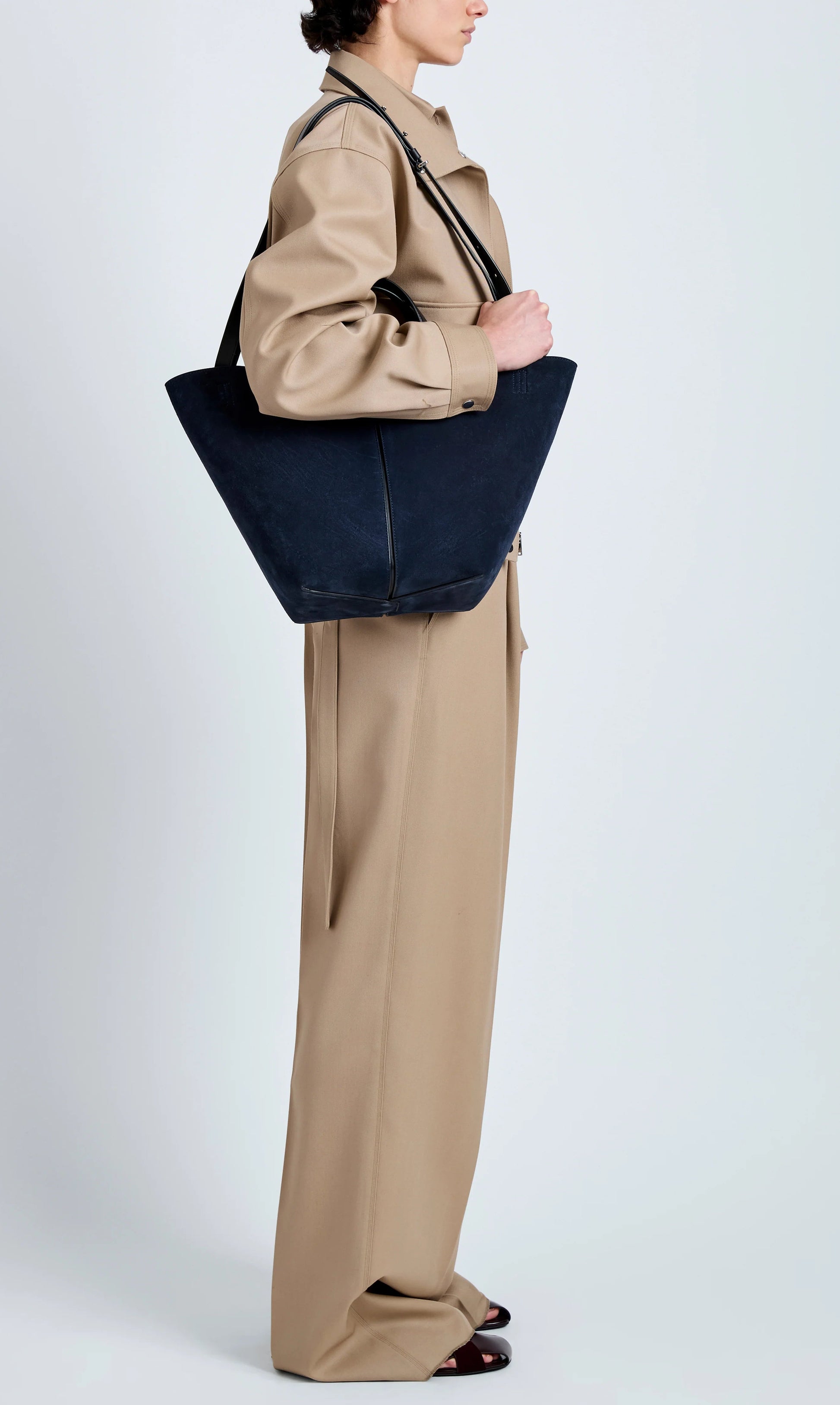 A person in a beige suit stands in profile with the Proenza Schouler Chelsea Large Soft Suede Tote over their shoulder against a plain light background.
