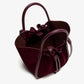 The Proenza Schouler Small Ruched Soft Suede Tote in burgundy features structured handles, a drawstring closure, an open top, and a sculptural silhouette—displayed on a plain white background.