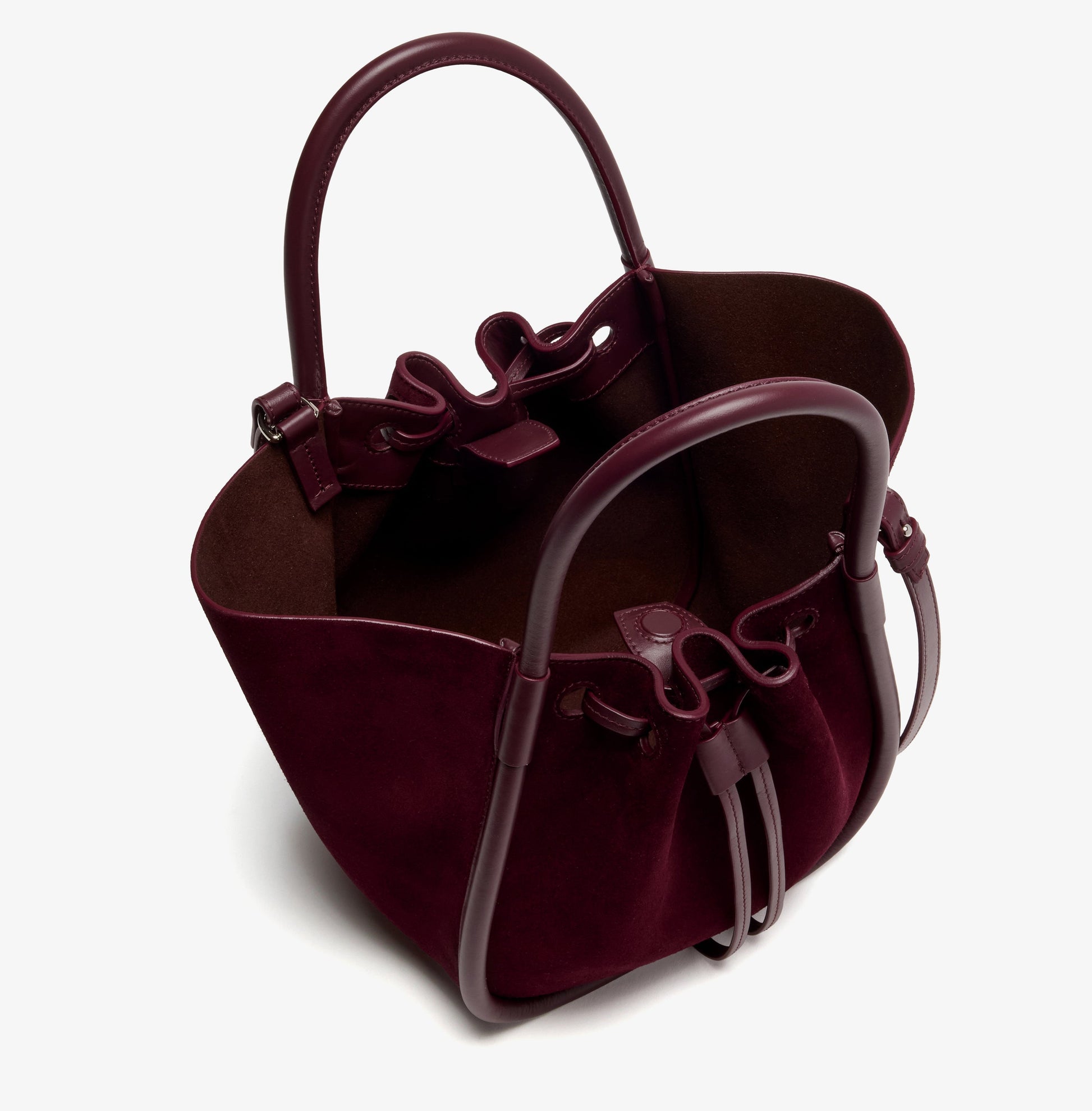 The Proenza Schouler Small Ruched Soft Suede Tote in burgundy features structured handles, a drawstring closure, an open top, and a sculptural silhouette—displayed on a plain white background.