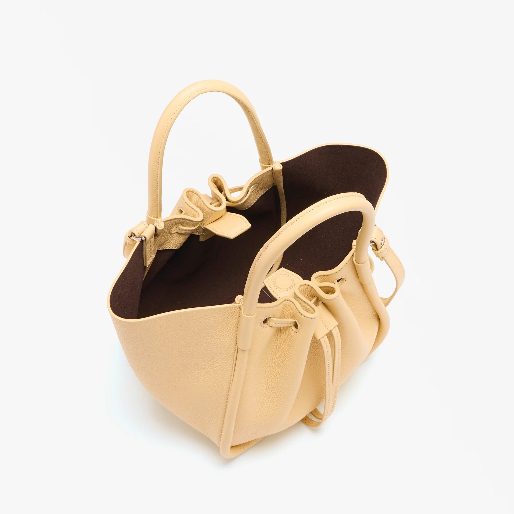 The Proenza Schouler Small Ruched Soft Pebbled Calf Tote features beige leather, a drawstring closure, dual handles, a dark brown interior, and a sculptural silhouette. Shown on a white background.