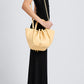A woman in a sleeveless black dress and white slip-on shoes, shown in profile, carries a light yellow Proenza Schouler Small Ruched Soft Pebbled Calf Tote with a sculptural silhouette.