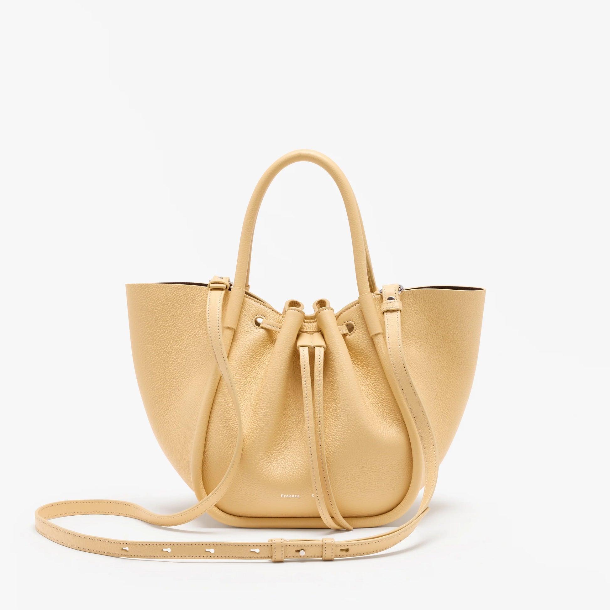 The Proenza Schouler Small Ruched Soft Pebbled Calf Tote is a beige leather bag with two handles, a drawstring closure, and an adjustable shoulder strap in a sculptural silhouette, shown against a plain white background.